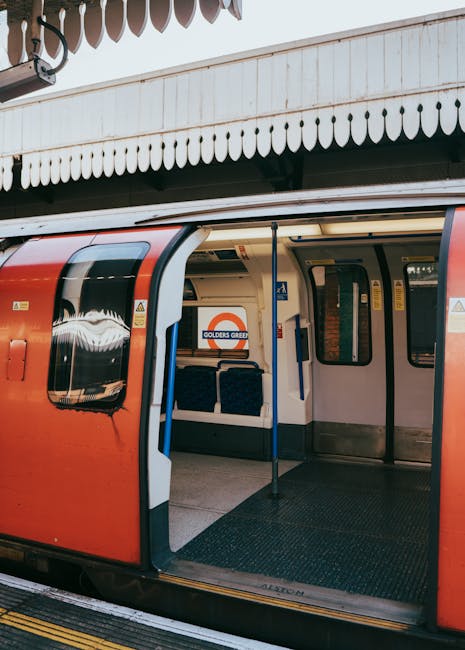 An underground train station platform with curved white-tiled walls and a black train tunnel in the distance. The platform has a tactile yellow safety strip along the edge and is equipped with metal b